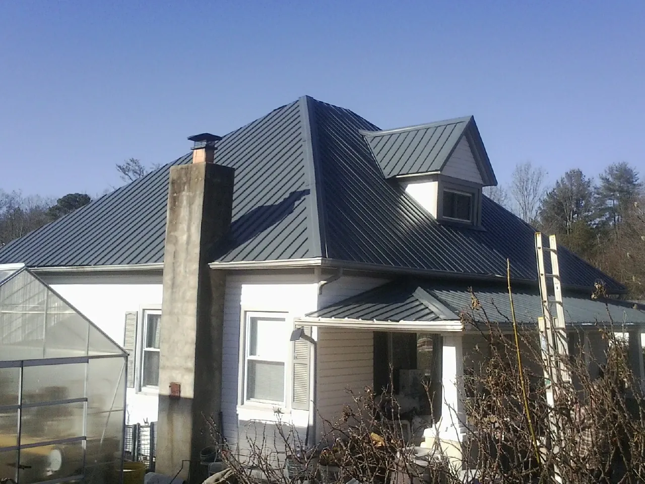 Dark blue standing seam metal roof on a white farmhouse with dormer — Slate & Tile Roof Repair by Roofing Brothers in Whitt