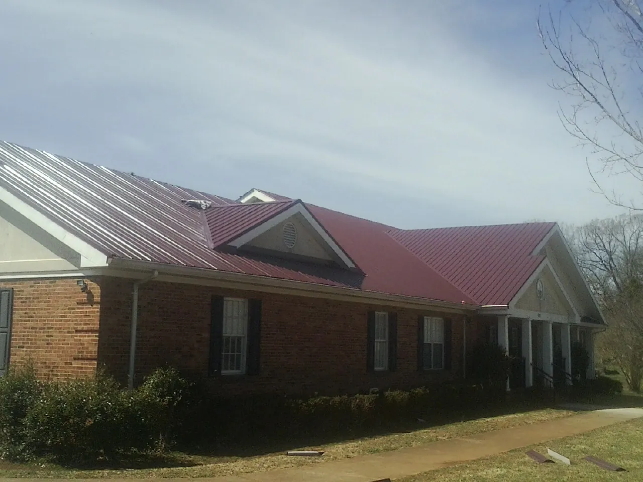 Red metal roof with gabled entries on a long brick building, from a Hail Damage Roof Repair job in Whitt