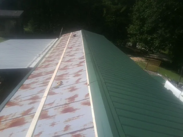 Old rusted panels beside newly installed green metal roofing — Wind Damage Roof Repair by Roofing Brothers in Whitt