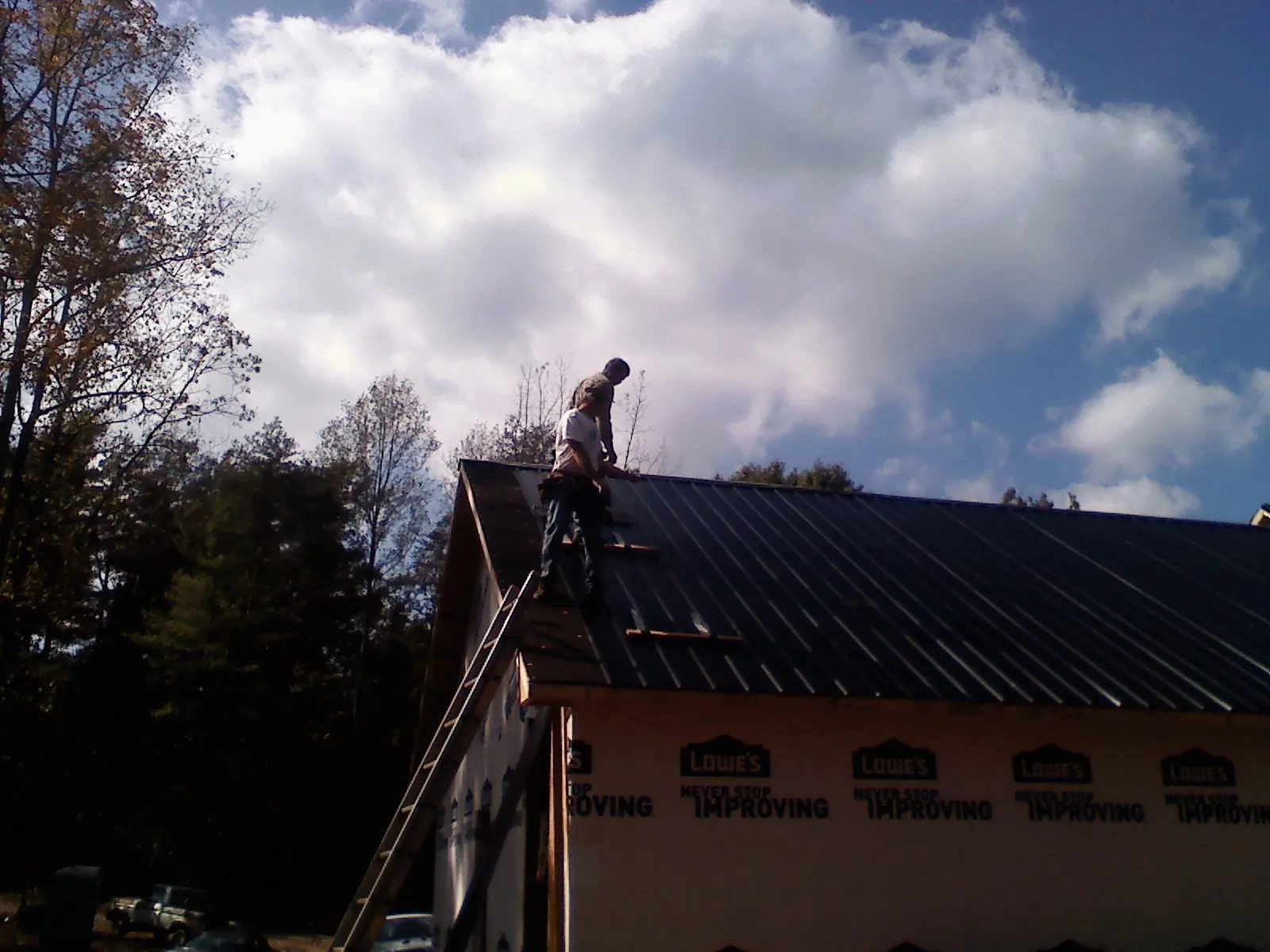 Roofer fastening dark metal panels high against a cloudy sky, from a Roof Inspection job in Whitt