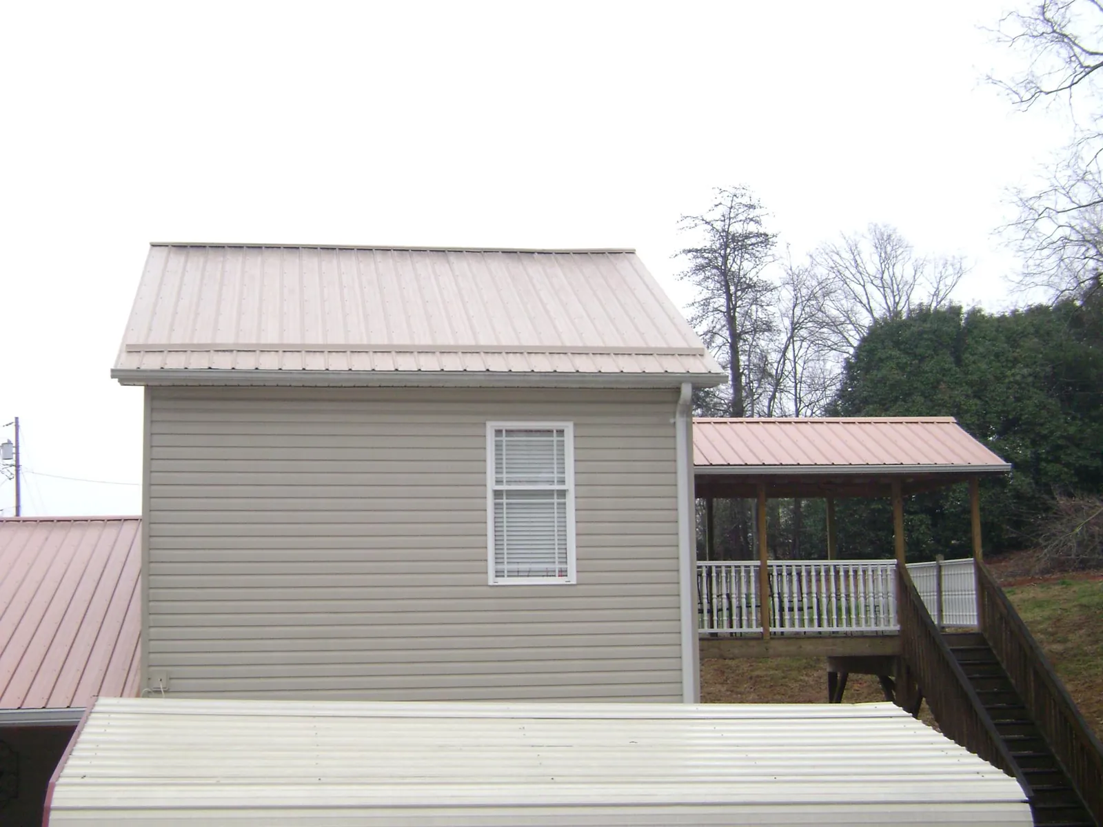 Tan metal roofs on a two story addition and attached porch, from a Roof Replacement job in Whitt